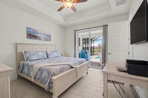 A bedroom with a bed, a desk, a ceiling fan, a painting, and a sliding glass door leading to an outdoor area. - Coral Oasis – Pet-Friendly Freshwater Canal (Cape Coral)
