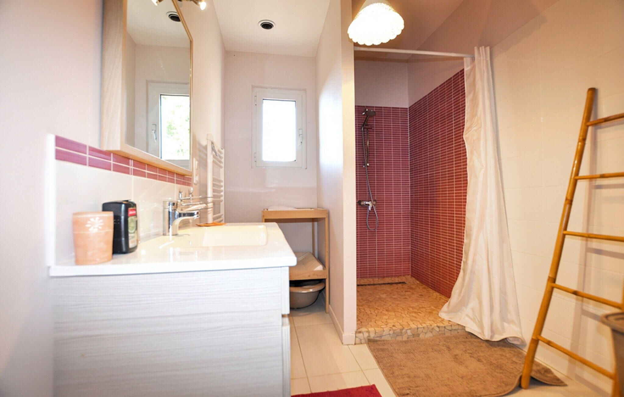 A bathroom with a white sink, mirror, and a shower with red tiles.