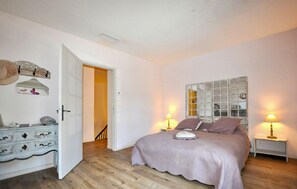 A bedroom with a bed, bedside lamps, a dresser, a mirror, and a door leading to another room.