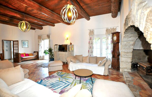 A cozy living room with a stone fireplace, wooden ceiling beams, a television, and a sofa set.