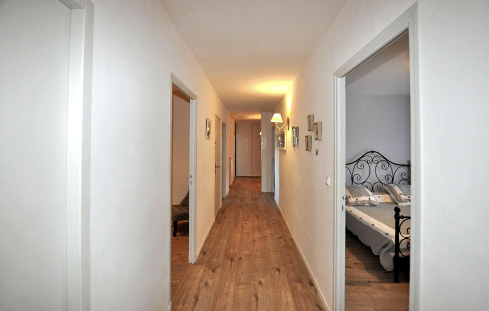 A narrow hallway with wooden flooring leading to a bedroom with a bed and a nightstand.