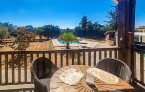 A balcony with wicker chairs, a round table, and a view of a swimming pool and trees. - Charmante maison avec piscine (Méjannes-lès-Alès)