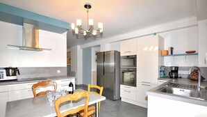 Uma cozinha moderna com área de refeições, eletrodomésticos de aço inoxidável e um lustre.