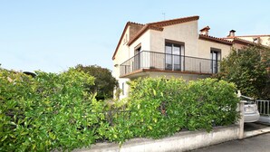 Um edifício de dois andares com varanda, rodeado por vegetação.
