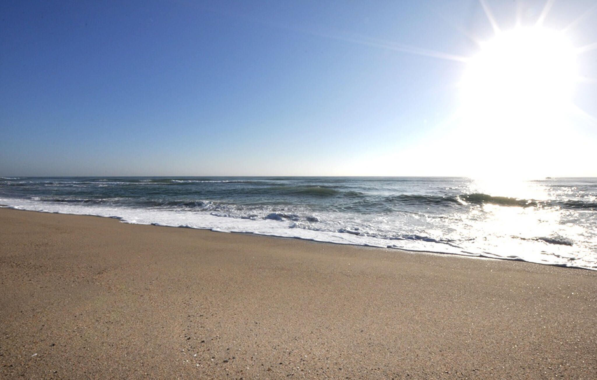 A beach with a clear sky and sunlight reflecting off the water.