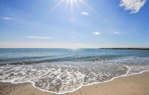 Una playa con olas, cielo despejado y costa rocosa.