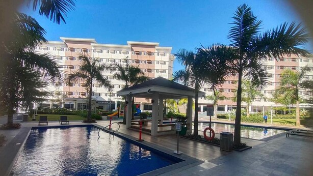 Une piscine avec un kiosque, des palmiers et un immeuble à plusieurs étages en arrière-plan.