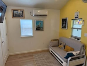 Un espacio habitable compacto con sofá, ventana y aire acondicionado instalado en la pared.