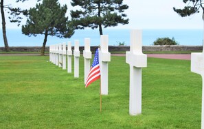 A row of white crosses on a grassy field with an American flag in front. - Maison zen proche littoral (LESSAY)