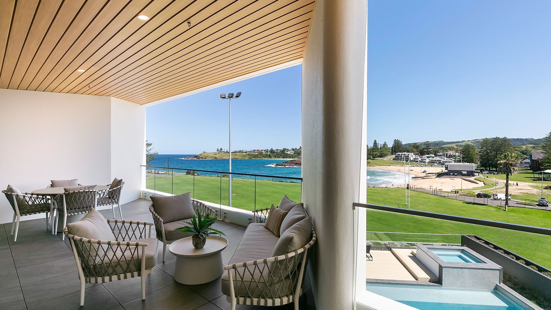 A balcony with a view of the sea, outdoor seating, and a pool.