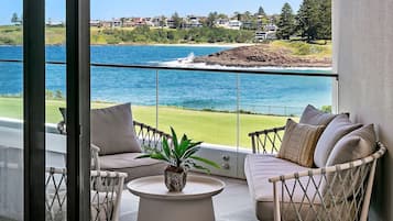 A balcony with a sofa, chairs, and a table, overlooking a body of water and a residential area.