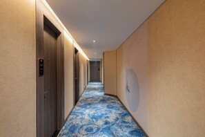 A hotel hallway with a patterned carpet, wooden doors, and a wall with a tree design. - TÂN PHƯƠNG NAM GALAXY (Da Nang)
