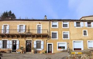 A two-story building with a balcony, a door with shutters, and a small garden area with potted plants. - Lovely home in St Julien du Gua with WiFi (St Julien du Gua)