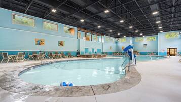 An indoor swimming pool with a tiled edge, surrounded by lounge chairs and a poolside area.