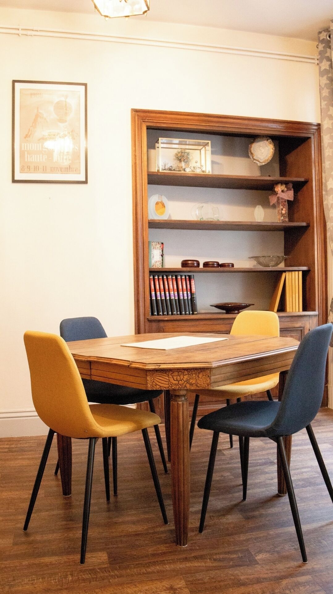 Un comedor con una mesa y sillas de madera, una estantería con libros y objetos decorativos, y un cuadro en la pared.