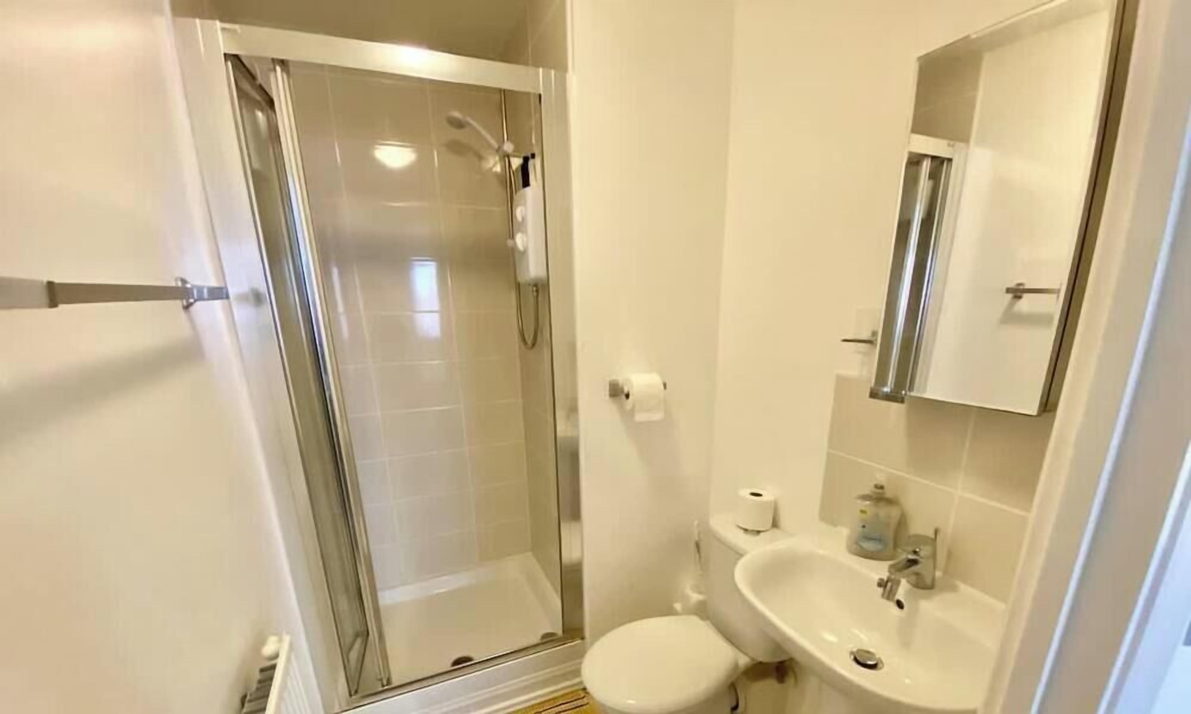 Een badkamer met een douchecabine van glas, een wastafel, toilet en een spiegel.