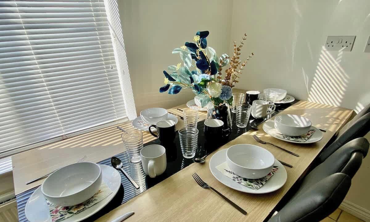 Een eettafel gedekt met borden, kommen, bekers en bestek, met een bloevas in het midden.