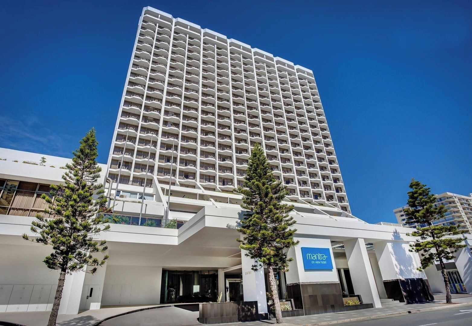 A tall hotel with a modern design, featuring a prominent entrance and a sign for 'Mantra on View Hotel.'