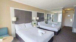 Ein Hotelzimmer mit zwei Betten, einem kleinen Tisch mit Pflanze und einem großen Spiegel.