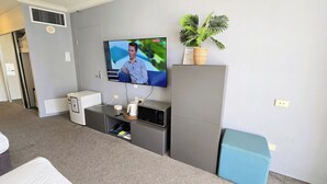 Ein Wohnzimmer mit Flachbildfernseher, kleinem Kühlschrank, Mikrowelle, einer Pflanze und einem blauen Sofa.