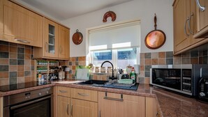Moderni keittiö, jossa on puiset kaapit, ruostumattomasta teräksestä valmistettu uuni, mikroaaltouuni ja ikkuna, josta on kaunis näkymä.