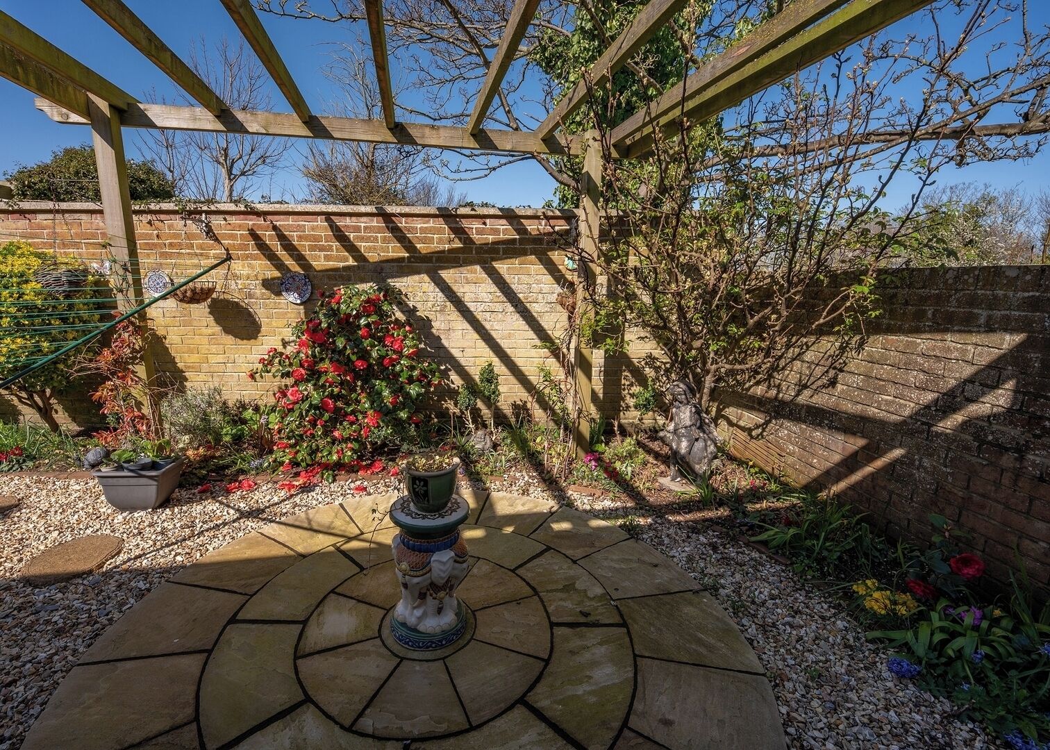 Un jardin agrémenté d’une pergola, d’un mur en briques et d’une statue.