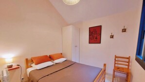 Un dormitorio con cama, una silla, un armario, una lámpara y un cuadro en la pared.