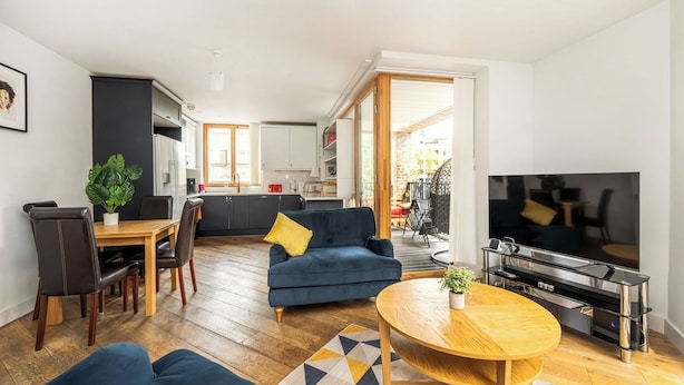 Una sala moderna con sofá, mesa de centro y televisor. Se aprecia un comedor con sillas y una mesa, y una cocina al fondo.