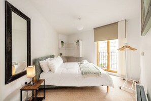 A bedroom with a bed, a bedside table, a mirror, a window with a view, and a hanging light fixture. - Cool 2BR Apartment with Air Conditioning! (London)