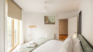 Un dormitorio con cama, un radiador, una lámpara colgante, una puerta y una ventana.