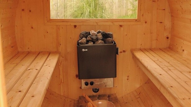 A sauna with wooden benches, a window, a sauna heater, and a wooden bucket. - Scenic 3BR Home with Sauna and Views (Warrenpoint, Newry)