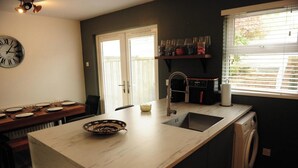 A kitchen with a marble countertop, a sink, a built-in washing machine, and a dining area with a table set for four. - Scenic 3BR Home with Sauna and Views (Warrenpoint, Newry)