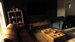 A living room with a sofa, a coffee table, a wooden cabinet, and a shelf with plants. - Scenic 3BR Home with Sauna and Views (Warrenpoint, Newry)