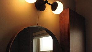 A circular mirror with a wooden frame, a wall-mounted light fixture above it, and a window in the mirror's reflection. - Scenic 3BR Home with Sauna and Views (Warrenpoint, Newry)