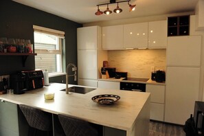 A compact kitchen with a central island, white cabinetry, a built-in oven, and a coffee machine. - Scenic 3BR Home with Sauna and Views (Warrenpoint, Newry)