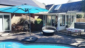 Un jardin avec une piscine, un patio couvert, un fauteuil de relaxation et une table.