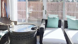 Une terrasse couverte avec un ventilateur de plafond, des meubles en osier et une vue sur le jardin arrière.