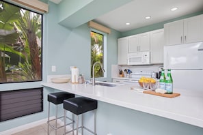A modern kitchen with white cabinets, a stainless steel refrigerator, and a large window with a view of greenery. - 3 Grand Champions | Treeline View | Sleeps 14 | Free Car w/ 6+ Nts | ML-3786 (Wailea)