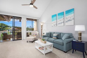 A spacious living room with a large window, a ceiling fan, a sofa, a coffee table, and a side table with a lamp. - 4 Grand Champions | Treeline View | Sleeps 20 | Free Car w/ 6+ Nts | ML-3789 (Wailea)