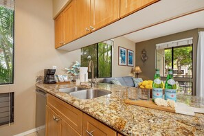 A kitchen with granite countertops, stainless steel sink, wooden cabinets, and a dining area with a table and chairs. - 4 Grand Champions | Treeline View | Sleeps 20 | Free Car w/ 6+ Nts | ML-3789 (Wailea)