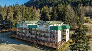 A multi-story hotel with balconies, surrounded by dense forest and mountains. - Ski-In Studio - Queen Murphy Bed - Walk to Lift (Girdwood)