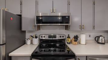 A kitchen with a stainless steel refrigerator, a microwave, an oven, and a stovetop. There are cabinets above the countertop, and a coffee maker is visible on the right.