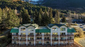 A multi-story hotel with balconies, surrounded by forest and mountains. - Ski-In Studio - Queen Murphy Bed - Walk to Lift (Girdwood)