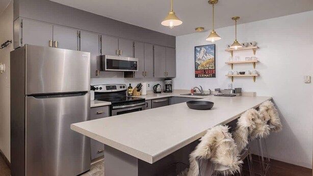A modern kitchen with stainless steel appliances, a white island, and pendant lighting. - Ski-In Studio - Queen Murphy Bed - Walk to Lift (Girdwood)