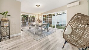 Un espace repas comprenant une table et des chaises, un fauteuil en osier et une vue sur l’extérieur.