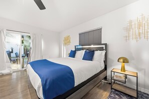 Ein modernes Schlafzimmer mit Bett, Nachttisch, Deckenventilator und Blick durch eine Glastür.