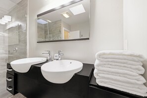 Ein Badezimmer mit zwei Waschbecken, einem Spiegel und einem Stapel weißer Handtücher.