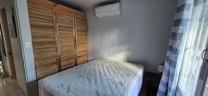 A bedroom with a bed, a wooden wardrobe, an air conditioning unit, and a window with a curtain. - Peaceful 2-bedroom house w/ AC in beautiful Playas del Coco, Guanacaste Province (Guanacaste Province)