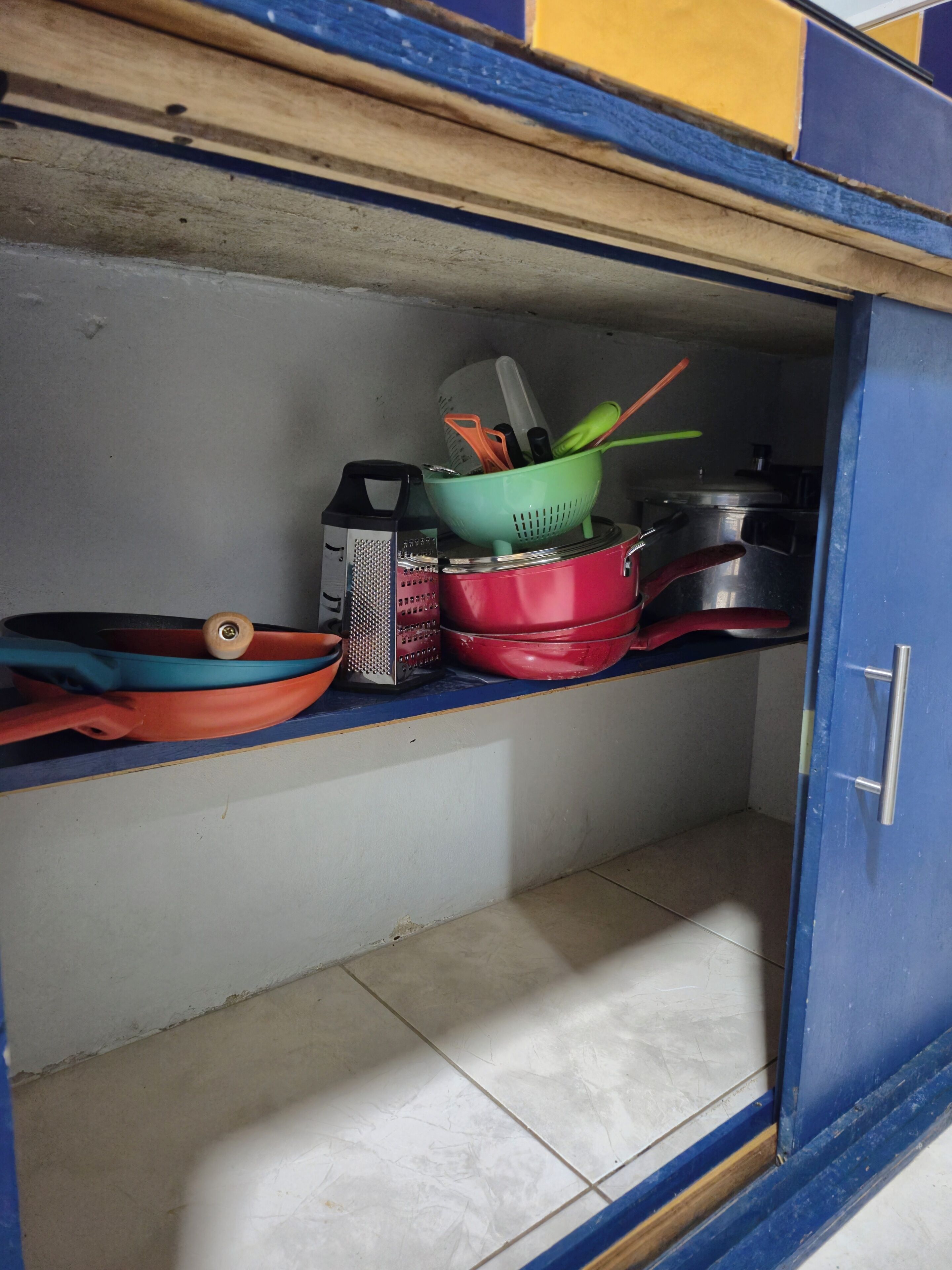Une cuisine avec un meuble bleu, une casserole rouge, une râpe et une passoire verte.