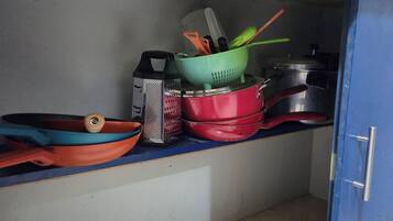 Une cuisine avec un meuble bleu, une casserole rouge, une râpe et une passoire verte.